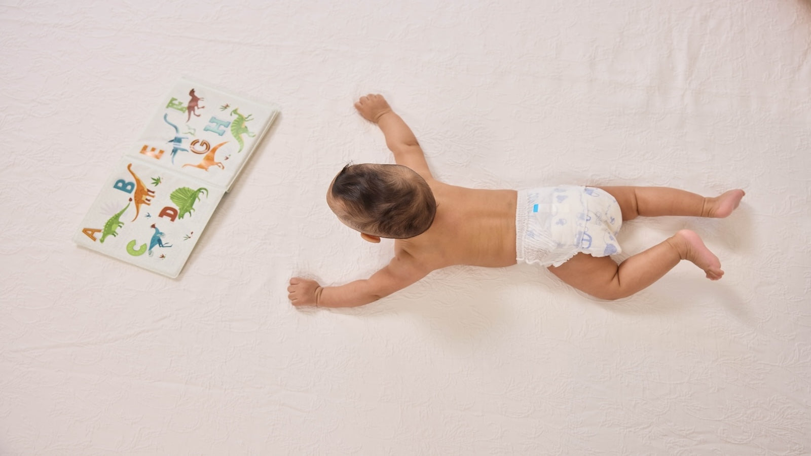 Baby in Pokito Pants on the bed with a book